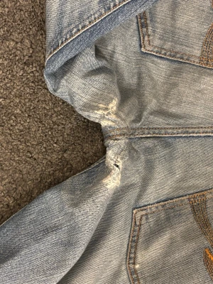 Ljusblå jeans från Nudie Jeans - Säljer nu mina älsklingar efter många användningar. Det är ett par ljusblå jeans från Nudie Jeans med klassiska bakfickor och slitna detaljer. Jeansen har raka ben, orange sömmar och är tillverkade i bomull. Perfekta för en avslappnad och trendig look. Jeansen har slutningar i fickorna som jag själv lagat så kan inte garantera att dem håller för evigt, samma vid knäet. Jeansen är uppsydda til ungefär 32 i längd