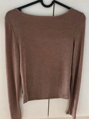 Brun långärmad topp i genomskynligt material - Mjuk och stilren brun långärmad topp i genomskynligt material. Enkel design med rund halsringning och rak passform. Perfekt att matcha med jeans eller kjol för en clean look.