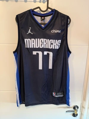 Dallas Mavericks Luka Dončić basketlinne - Snyggt basketlinne från Dallas Mavericks med Luka Dončićs nummer 77. Linnet är mörkblått med vita och blå detaljer, har ärmlös design och V-ringning. Tillverkat i lätt och ventilerande material, perfekt för basket eller streetwear.