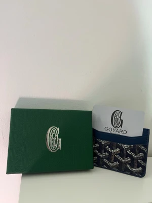 Plånbok - Snygg blå korthållare från GP med det klassiska vita och gråa mönstret. Tillverkad i canvas med läderdetaljer och har plats för flera kort. Perfekt för dig som vill ha något stilrent och exklusivt i fickan. Kommer med original grön ask. Den är väldigt smidig då den är liten, funkar till alla säsonger och är en perfekt plånbok/korthållare. Vi är två seriösa säljare från Skåne. Hör gärna av er vid minsta lilla fråga!🫡