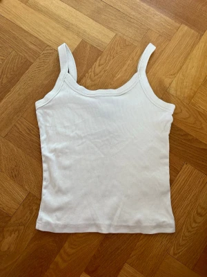 Beige ribbad linnetopp - Säljer en enkel och stilren beige ribbad linnetopp med smala axelband. Perfekt att matcha med jeans eller kjol för en clean look. Materialet är mjukt och stretchigt för skön passform.