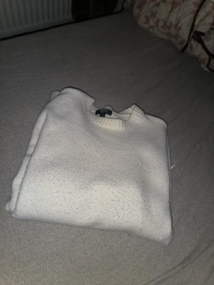 Vit stickad tröja från H&M - Klassisk vit stickad tröja från H&M med rund halsringning och ribbade muddar vid ärmslut och nederkant. Tröjan har en enkel och stilren design, perfekt för lager på lager och passar till det mesta. Materialet ser mjukt och bekvämt ut.