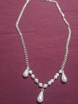 Silverfärgat halsband med pärldroppar - Snyggt handgjort halsband i silverfärgat rostfritt stål med metallfåsten där vita pärlor och tre droppformade pärlor hänger framtill. Kedjan är tunn och smidig, och pärlorna ger en elegant touch. Perfekt accessoar för att lyfta din outfit.