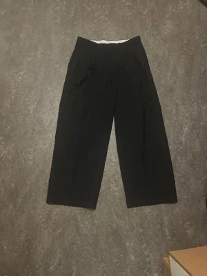 Svarta vida kostymbyxor - Säljer ett par svarta kostymbyxor från Weekday lös passform med veck. Använda max 6 gånger i mycket bra skick. Baggy passform med pressade veck som ger en mer dressad känsla. Säljer då de inte passar mig längre.