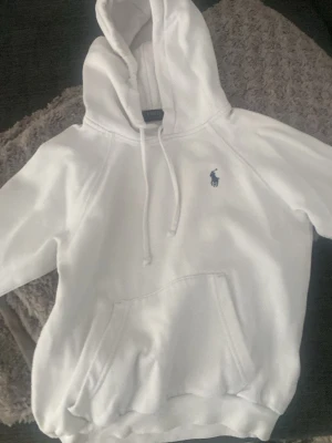 Vit hoodie från Polo Ralph Lauren xxs  - Tja Säljer en clean vit hoodie från Polo Ralph Lauren med klassisk blå logga på bröstet. Hoodien har huva med dragsko, stor magficka och ribbade muddar. Perfekt till jeans eller sweatpants för en chill look. För den är för liten storlekar xxs eller xs  passar om du är 150 eller lite kortare och längre 