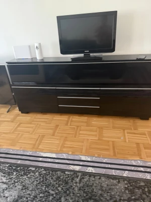  Tv byggen är nytt - Säljer en modern svart tv-bänk med högblank finish och flera rymliga lådor. Bänken har raka linjer och silverfärgade handtag som ger ett stilrent intryck. Perfekt för förvaring av elektronik och annat i vardagsrummet.