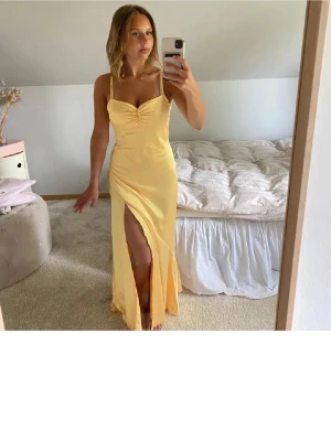 balklänning - Säljer en ljusgul långklänning med smala axelband och snygg slits framtill. Klänningen har en v-ringad överdel med rynkdetalj vid bysten och är figurnära i passformen. Perfekt för sommarens alla tillfällen! hon på bilderna är ca 164 cm😊
