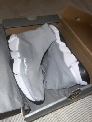 Grå Balenciaga Speed Trainer sneakers - Säljer ett par grå Balenciaga Speed Trainer sneakers med vit och svart chunky sula. Skorna har en strumpliknande ovandel i stretchigt tyg och Balenciaga-logga på sidan. Perfekta för dig som gillar en modern och sportig look.