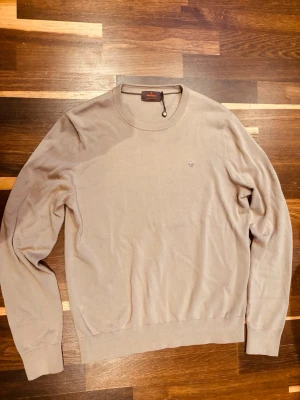 Beige tröja från Morris - Stilren beige tröja från Morris med rund halsringning och diskret broderad logga på bröstet tröjan är i näst intil nyskick och är perfekt för vår och sommar 