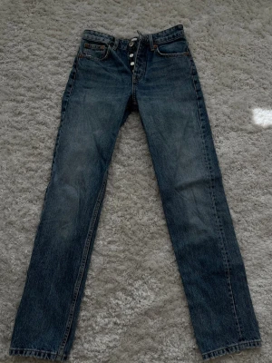 Blå raka midrise jeans från Zara - Snygga blå jeans från Zara med raka ben och hög midja. Klassisk femficksmodell med knappgylf och kontrastsömmar. Tillverkade i slitstark denim som ger en tidlös look. Perfekta för dig som gillar en enkel och clean stil.