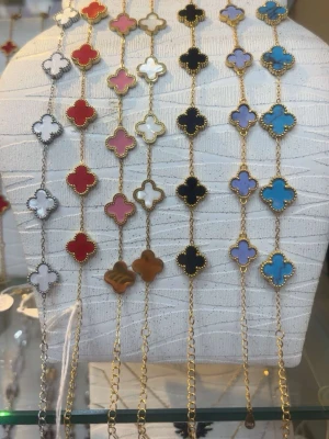 Färgglada fyrklöverarmband i guld - Säljer flera armband med fyrklöverformade hängen i olika färger som rött, vitt, rosa, svart, blått, lila och brunt. Armbanden har guldfärgade kedjor och detaljer runt varje hänge. Perfekta för att addera färg och stil till din outfit.