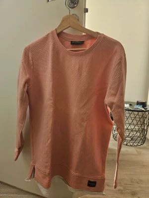 Rosa sweatshirt - Säljer en ljusrosa långärmad topp från Machinist. Toppen har rund halsringning, slitsar i sidorna och är gjord i ett ribbat bomullsliknande material. Som ny, endast använd 2-3 gånger och nu är storleken liten för mig.