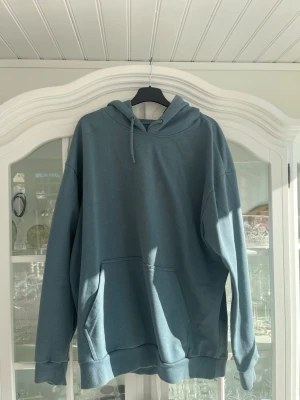Blå hoodie från 157 med huva - Snygg  hoodie från 157 med klassisk känguruficka och dragsko i huvan. Tillverkad i mjukt material som känns skönt mot huden. Perfekt för dig som gillar en enkel och clean stil. Passar till det mesta och är lätt att matcha.