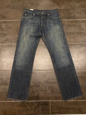 Mörkblå raka jeans från Hugo Boss - Säljer ett par mörkblå jeans från Hugo Boss med raka ben och klassisk femficksmodell. Jeansen har snygga slitningar framtill och kontrastsömmar. Tillverkade i slitstark denim som ger en cool och tidlös look. Storlek 33/34