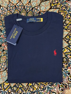Mörkblå t-shirt från Polo Ralph Lauren - Snygg mörkblå t-shirt från Polo Ralph Lauren med klassisk röd broderad logga på bröstet. Tillverkad i mjuk bomull och har en normal passform med korta ärmar. Perfekt basplagg för en clean och stilren look.