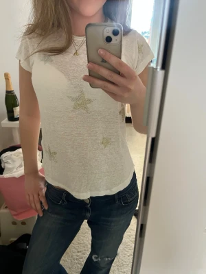 Vit t-shirt med stjärnor - Säljer en vit, tunn t-shirt med glittriga stjärnor framtill. T-shirten har korta ärmar och en rund halsringning. Materialet känns lätt och luftigt, perfekt för varmare dagar. T-shirten är från Zadig & Voltaire och är endast använd ett par fåtal gånger💞