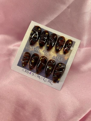 DarkSyrup (S);Medium Almond - Snygga handgjorda press-on naglar i brun marmorerad look med vita swirl-mönster och små guldiga stjärnor och guldpärlor. Formen är medium almond. Perfekt för dig som vill ha unika och trendiga naglar utan att gå till salong. S: 15 mm, 11,5 mm, 12 mm, 11 mm, 9 mm 