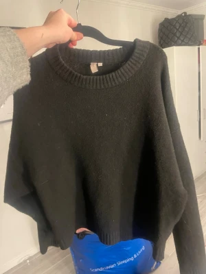 Svart stickad tröja med rund hals - En svart stickad tröja med avslappnad passform och rund halsringning. Tröjan har ribbade muddar vid hals, ärmslut och nederkant. Perfekt för lager på lager och enkel att matcha med olika outfits.