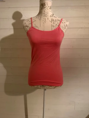 Rosa linnetopp med smala axelband - En enkel och stilren rosa linnetopp med smala axelband. Toppen har en tight passform och är tillverkad i mjukt bomullsmaterial, perfekt för varma dagar eller som lager under andra plagg.