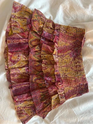 Mönstrad volangkjol från Zara - Trendig och eftertraktad kort kjol från Zara med flera volanger och ett färgstarkt paisleymönster i rött, gult och rosa. ❤️