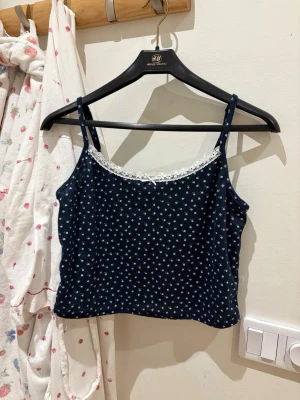 Mörkblå blommig linnetopp med spets - Söt mörkblå linnetopp från H&M med små vita blommor och tunna axelband. Toppen har en fin spetskant längs urringningen som ger en extra detalj. Perfekt för varma dagar eller att styla lager på lager.