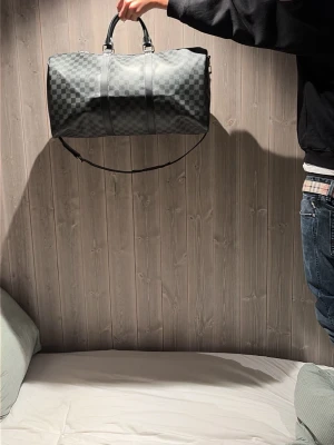 Louis Vuitton svart damier weekendbag - Snygg weekendbag från Louis Vuitton i svart och grått damier-mönster. Väskan har dubbla handtag, avtagbar axelrem och silverfärgade metalldetaljer. Perfekt storlek för resor och har en klassisk, lyxig look. Tillverkad i slitstarkt canvasmaterial.