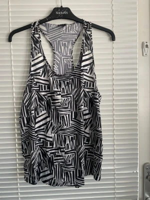 Svartvit mönstrad linnetopp Gina Tricot - Säljer en svartvit linnetopp från Gina Tricot med coolt grafiskt mönster. Toppen är ärmlös med brottarrygg och har en loose passform som känns riktigt chill och luftig. Perfekt till sommaren eller när du vill ha en avslappnad vibe. Känns inte som en L utan mer som M