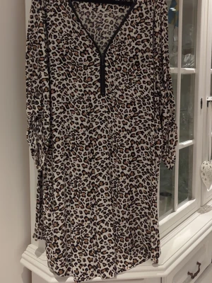 Leopardmönstrad klänning från Isolde - Leopardmönstrad klänning från Isolde med dragkedja framtill och v-ringad hals. Klänningen har långa ärmar och är i ett lätt, mjukt material som känns skönt mot huden. Perfekt för dig som vill sticka ut med ett djurmönster.