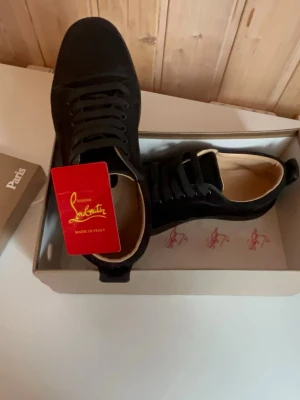 Svarta sneakers från Christian Louboutin - Snygga svarta sneakers från Christian Louboutin med klassisk låg siluett. Skorna har svart ovandel i mocka och matchande svarta skosnören. Insidan är beige och de kommer i originalkartong med logga. Perfekta för dig som vill ha något exklusivt och stilrent. Skicka 1-3 dagar!