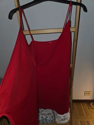 Röd omlottklänning med knyt - Snygg röd kortklänning med omlott-design och knyt i sidan. Klänningen har smala axelband och v-ringad fram. Perfekt för dig som vill ha en enkel men stilren look. Materialet känns mjukt och lätt, troligen polyester. Står tyvärr ingen storlek men är lite stor för mig och jag är en S, skulle tippa på att de passar M.