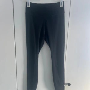 Svarta leggings med hög midja - Säljer ett par svarta leggings med hög midja och tight passform. Dem har en klassiskoch enkel design med ett Nike märke nere på vänstra benet. Perfekta för en clean och stilren look.