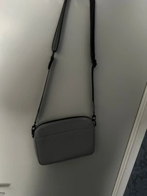 Grå axelväska från Louis Vuitton - Snygg grå axelväska från Louis Vuitton med klassiskt monogrammönster i präglat läder. Väskan har en justerbar axelrem och stilren, rektangulär form. Perfekt för dig som vill ha en trendig och exklusiv accessoar till din outfit.