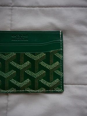 GYRD | Korthållare - Snyggt grönt kortfodral med det klassiska mönstret i vitt och brunt. Fodralet har flera kortfack och är gjort i läder med detaljerad sömnad. Perfekt för dig som vill ha en stilren och exklusiv accessoar i fickan. Kommer med originalförpackning, knappast använd! Nypris 5000sek.