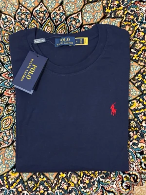 Mörkblå t-shirt från Polo Ralph Lauren - Snygg mörkblå t-shirt från Polo Ralph Lauren med klassisk röd broderad logga på bröstet. Tillverkad i mjuk bomull och har en normal passform med korta ärmar. Perfekt basplagg för en clean och stilren look.