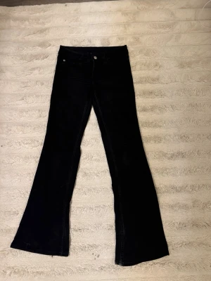 Svarta bootcut jeans - Säljer ett par svarta bootcut jeans med klassisk femficksdesign och utsvängda ben. Jeansen har normal midja och stängs med knapp och dragkedja. Perfekta för dig som gillar en retroinspirerad look.
