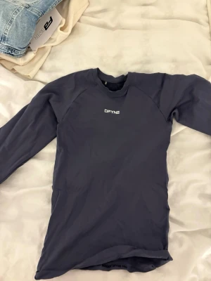 Mörkblå långärmad tröja från DFYNE - Snygg mörkblå långärmad tröja från DFYNE med enkel design och vit logga på bröstet. Tillverkad i ett stretchigt och mjukt material som sitter skönt på kroppen.