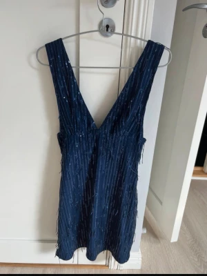 Mörkblå glittrig kortklänning - Snygg mörkblå kortklänning med djup v-ringning både fram och bak. Klänningen har glittriga detaljer i tyget som ger en festlig känsla. Klänningen är från SHEIN med prislapp på! Aldrig använt 