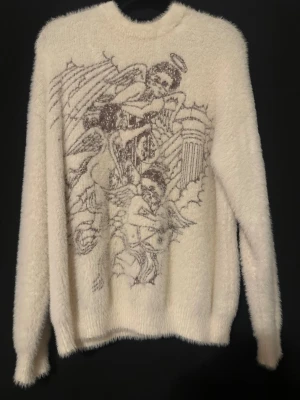 Mohair tröja unisex - Mysig vit stickad tröja med fluffig textur och ett stort motiv av änglar och pelare framtill. Tröjan har rund halsringning och långa ärmar. Perfekt för dig som gillar unika och konstnärliga plagg med vintage vibe.