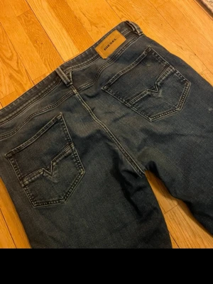 Mörkblå jeans från Diesel - Snygga mörkblå jeans från Diesel med klassisk femficksmodell och raka ben. Jeansen är i bra skick förutom ett litet hål vid gylfen. Bakfickor med V-formad söm. Tillverkade i denim med en cool tvätt och läderpatch med logga bak i midjan.