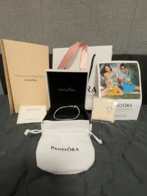 Pandora silverarmband med hjärtformad lås - Säljer ett snyggt silverfärgat armband från Pandora med ett hjärtformat lås. Armbandet har en klassisk ormkedjedesign och är perfekt för att addera egna berlocker. Kommer med originalpåse, ask och certifikat.