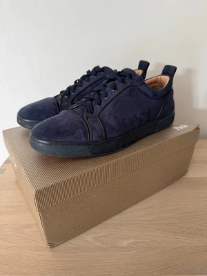 Mörkblå sneakers från Christian Louboutin - Snygga mörkblå sneakers i mocka från Christian Louboutin med klassisk röd sula. Skorna har svarta snören, svarta detaljer och låg profil. Perfekta för dig som vill sticka ut med exklusiva och stilrena sneakers storlek 40-41
