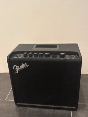 Fender Mustang LT25 Förstärkare - Säljer en svart bärbar högtalare från Fender med flera reglage och knappar på ovansidan. Högtalaren har en rektangulär form, bärhandtag och är klädd i ett tåligt material. Perfekt för att spela musik eller använda till instrument.