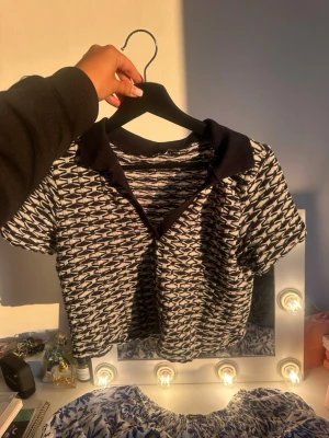 Mönstrad kortärmad topp från Zara - Kortärmad topp från Zara med svartvitt mönster och krage i mörkare ton. Toppen har en croppad passform och är tillverkad i ett stickat material som ger en cool struktur. Perfekt för dig som gillar unika detaljer och trendig stil.