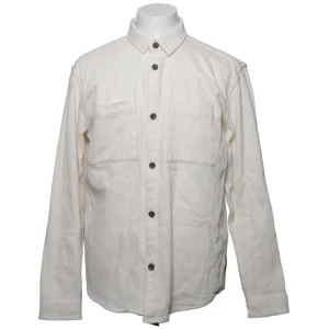 Vit overshirt med fickor - Stilren vit overshirt med raka linjer och två bröstfickor. Skjortan har svarta knappar framtill och vid ärmsluten samt klassisk krage. Tillverkad i ett kraftigare bomullstyg som ger en avslappnad men ändå snygg look.