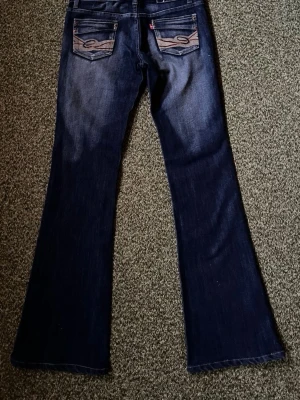 Mörk blåa bootcut med detaljerad bakfickor  - Mörk blåa kvarg aktig bootcut jeans med detaljer på fickorna i storlek W27 så det passar XS-S