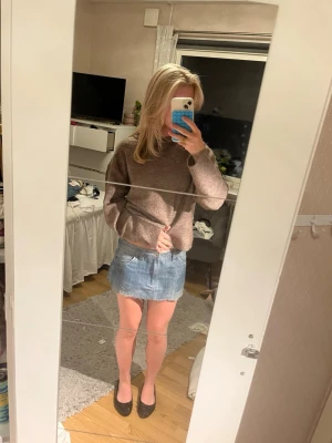 Blå jeanskjol med broderade fickor - Kort blå jeanskjol i klassisk modell med två stora fickor bak. Kjolen har en rak passform och rå kant nertill för en avslappnad look. Perfekt att matcha med en stickad tröja eller t-shirt, säljs då den är lite stor och inte används.