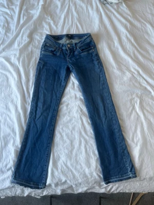 Blå bootcut jeans med låg midja - Snygga blå bootcut jeans med låg midja och klassiska fem fickor. Jeansen har en lätt utsvängd passform nedtill och är tillverkade i ett mjukt denimtyg. Perfekta för en avslappnad och trendig look. Nypris: 799 men pris ej hugget i sten. 