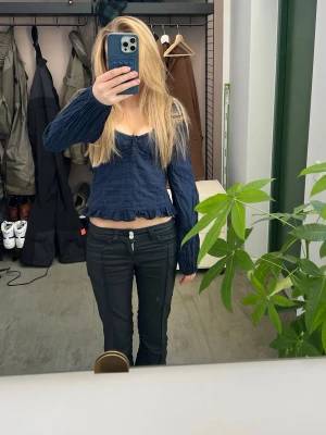 Mörkblå långärmad blus med volang - Säljer en mörkblå långärmad blus med v-ringning och knappar framtill. Toppen har en croppad passform och volangkant nedtill. Perfekt att styla med jeans eller kjol.