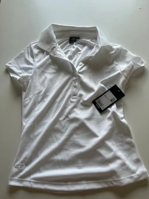 Vit kortärmad golf polotopp - Snygg vit polotopp med krage och knappar framtill. Tillverkad i ett lätt och svalt material, perfekt för varma dagar. Klassisk passform och korta ärmar ger en sportig look. Diskret logga nertill på sidan.