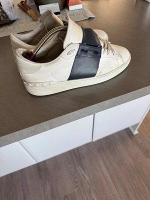 Valentino Garavani sneakers vit/blå - Säljer ett par snygga Valentino Garavani sneakers Perfekta för dig som gillar stilrena och exklusiva sneakers. Storlek 42. Pris kan diskuteras. Box och nya sulor följer med💯 tyvärr under är det hål på undersulan 